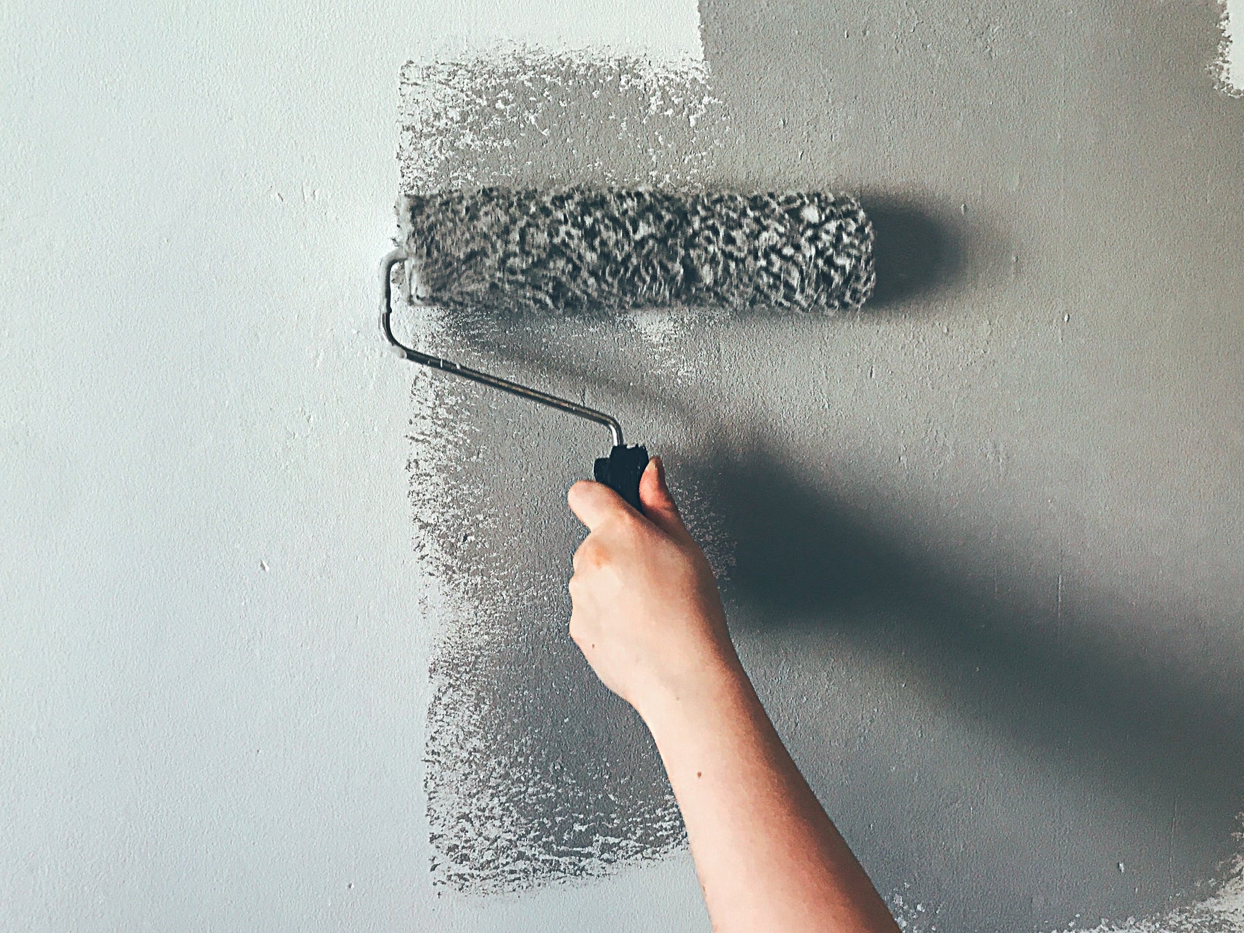 Streichrolle trägt graue Farbe auf Wand auf