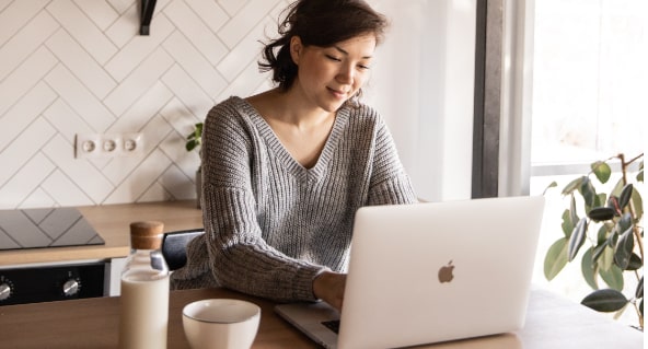 Frau sitzt am Tisch und tippt etwas auf ihrem Laptop