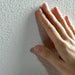 Hand beruehrt frisch gestrichene Wand und fuehlt die Struktur von AlpenKalk Rollputz